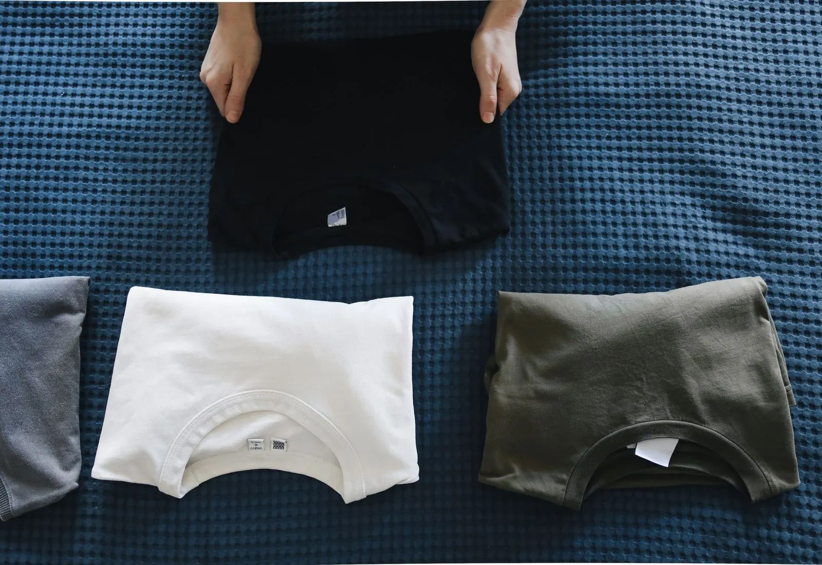 Folded t-shirts in black, white and olive laid out side by side
